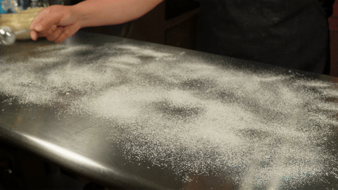 Demonstrates rolling out the dough and spreading the cinnamon filling.