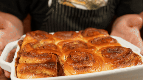 Demonstrates pouring glaze over the baked cinnamon rolls.