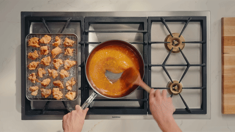 Shows tossing the fried chicken in the prepared sauce.