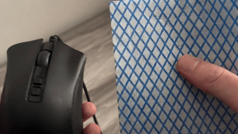 Demonstrates using a cloth to clean the gaps around the mouse wheel.