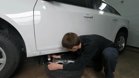 Demonstrates using a scissor jack to break the tire bead.