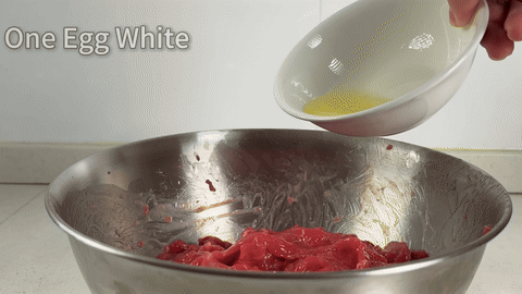 Shows the addition of egg white and cornstarch to the beef.